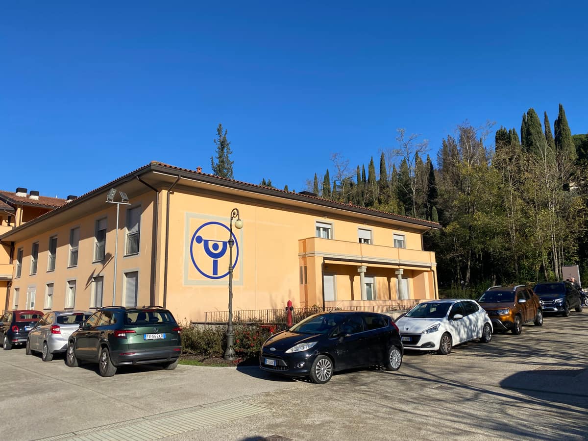 The ochre facade of Istituto Prosperius Fiesole, marked with the Prosperius logo, cypresses on the hillside behind