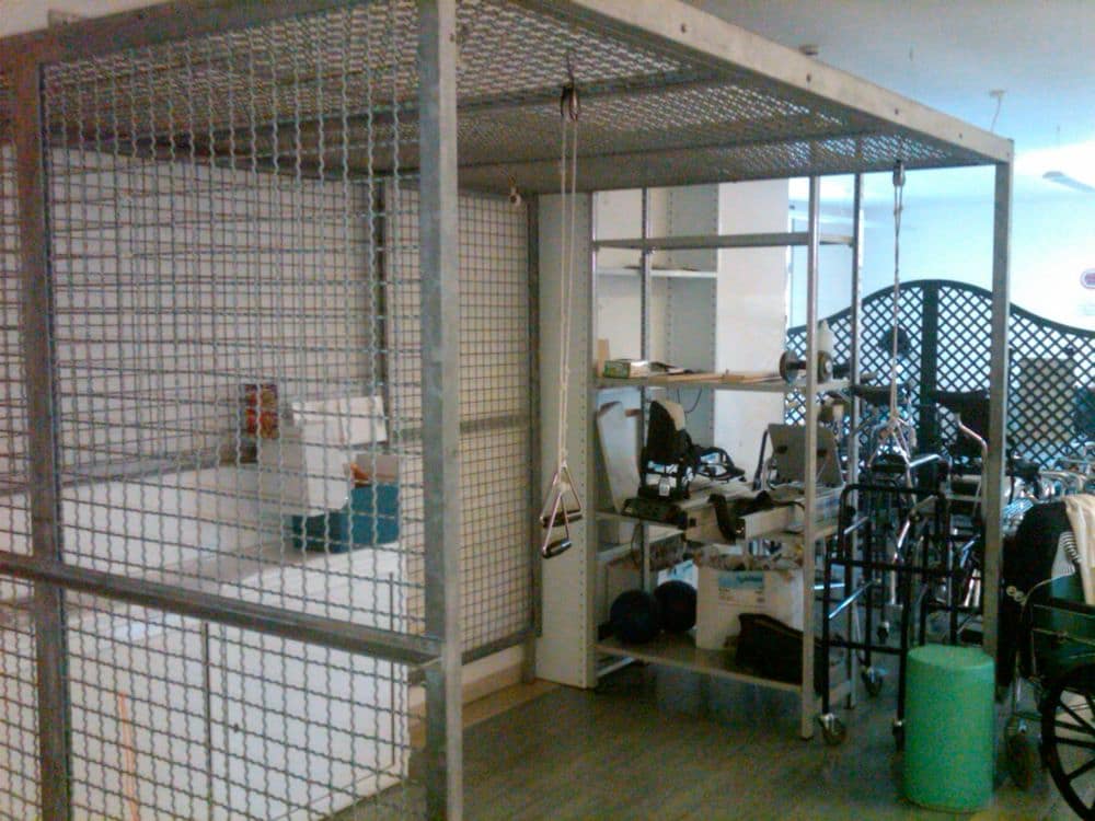 An equipment store at Istituto Clinico Tiberino: a steel rehabilitation frame hung with suspension straps, beside walking frames and wheelchairs