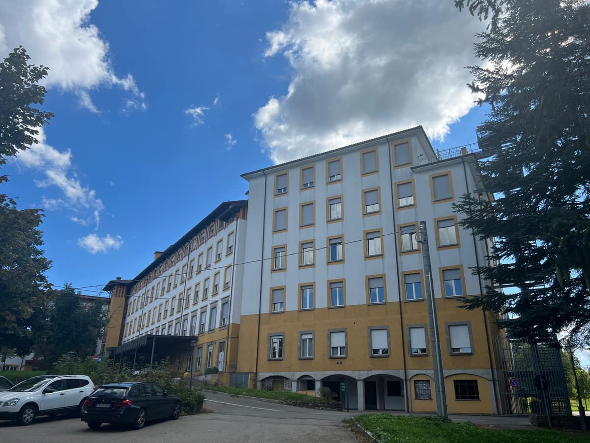 Villa Pineta seen from the road: a long five-storey hospital in white and ochre, wooded hills around it