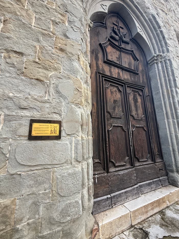 An old studded wooden door with a brass plaque set into the stone beside it